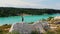 Landscape of a light blue lake surrounded by forest - a successful man running on a rock and raises his hands up