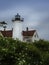 Landscape with lighthouse close-up over the wild rose flower bushes on blue soft cloudy sky backgrounds