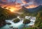 Landscape with majestic mountains, lush greenery, cascading waterfalls at sunset