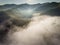 Landscape misty panorama. Fantastic dreamy sunrise on rocky mountains with view into misty valley below. Foggy clouds above