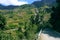 Landscape with mountains, forest and pines, cottages, mountain houses, blue sky, clouds, twisting road & terrace farms.