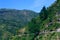 Landscape with mountains, forest and pines, cottages, mountain houses, blue sky, clouds, twisting road & terrace farms.