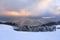 Landscape with mountains, snowy forest and beautiful sunrise. Majestic winter scenery. Dramatic sky. Meadow covered with snow.