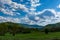 A landscape of nature with sunlit hills and meadows, accompanied by white fluffy clouds in the sky on a sunny spring day