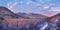 A landscape panorama of a South African valley full of fynbos plants and surrounded by low mountain peaks, the last of the sun