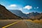 A landscape photo of the mountains, clouds, blue sky and large rocks taken from the middle of the road in Oman