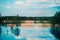 This landscape photo showcases the beauty of a blue cloudy sky, lush forests, sandy shores, and a crystal-clear lake reflecting it