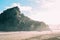 Landscape from the Piha beach with people walking around a high rock under bright sunlight