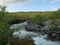 Landscape with rapids of wild blue glaciar river Kamajakka, rock, birch tree, green mountains at Rovvidievva sami village, Lapland