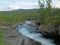 Landscape with rapids of wild blue glaciar river Kamajakka, rock, birch tree, green mountains at Rovvidievva sami village, Lapland