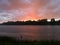 Landscape with river, colorful clouds and forested shore at sunset. Calm riverine scene during overcast dusk with rain or summer