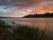 Landscape with river, colorful clouds, tall water grass and mountain in distance at sunset. Dramatic riverine scene during cloudy