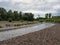 Landscape of river Ukrine, fast water current eroding gravel shore, riverbank overgrown with green bushes and trees during