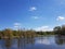 Landscape. The river on which are displayed green trees that grow in the shoreline. Blue sky with shelves. The soil is covered wi