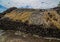 Landscape shot of golden-brown hays placed at the top of bedrock with a cloudy sky