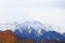 Landscape of the snow-capped mountains of the Trans-Ili Alatau behind thickets of autumn trees in cloudy weather