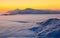 The landscape with a stunning sunset, interesting thick fog and mountains covered with textured snow on a winter day.