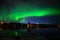 A landscape view of aurora borealis with a city scape under starry clear sky and reflection from lake water