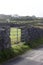 Landscape view of a gate and stone wall along paved road on the rugged terrain of Inishmore Island in Ireland