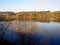 Landscape view of a large lake with trees in the foreground and forests, field and pastures in the backgrond