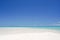 Landscape of a white sandy beach leading into turquoise waters under a blue sky on the island of Fakarava in French Polynesia