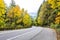 Landscape with a winding road with a marked dividing strip and a protective fence around the bend in a yellow autumn forest