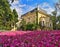 Landscape with yellow baroque house surrounded by green trees and a field of pink blossomed flowers