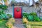 Landscaped garden with pathway inside white fence and red gate with pergola