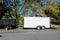 A landscaping truck with a long white enclosed trailer trailer seen on a shady residential asphalt street