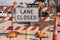 Lane Closed sign at messy construction urban intersection with sand bags traffic cones heavy equipment working and cars stopped at