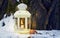 Lantern with candle in forest on snow near tree in evening. New Year celebration in nature_