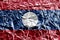 Laos flag depicted in paint colors on shiny crumpled aluminium foil closeup. Textured banner on rough background