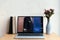 laptop with booking website on screen books and flowers in vase on wooden