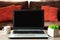 Laptop and coffee cup on wooden table against defocused sofa with pillows. Front view. Mock-up