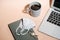 Laptop, coffee, medical mask, notebook and keys on a peach colored surface