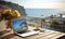 Laptop and a cup of coffee on table on a balcony with ocean view with copy space