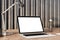 Laptop with desk lamp and glass bottle on wooden table against striped backdrop.