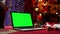 Laptop with green screen chroma key stands on red table next to Santa Claus, gifts and toys. Home room with Christmas