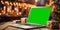 Laptop with green screen on wooden table with gift boxes against festive golden bokeh background. Mockup, chroma key, gadget