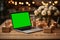 Laptop with green screen on wooden table with gift boxes, candles, flowers against festive golden bokeh background. Mockup, chroma