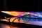 A laptop half closed in the dark with colourful glow and glasses.