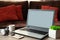 Laptop, headphones, smartphones. and coffee cup on wooden table against defocused sofa with pillows. Front view. Mock-up