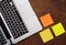Laptop keyboard and yellow and orange stickers on wooden background, view from above, flat lay, copyspace