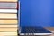 Laptop next to a stack of colorful books on a wooden table on a blue background