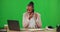 Laptop, phone call and black woman typing on green screen in studio isolated on a background. Cellphone, computer and