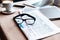 Laptop and smartphone, cup of coffee, documents, newspaper and glasses on table