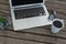 Laptop, spectacles, black coffee and pot plant on wooden plank