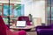 Laptop on a table with pink and purple chairs and office in the background