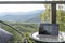 Laptop on wooden terrace, mountains and trees blurred as a background.