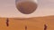 Large Alien Silver Sphere Floating above Desert Sand Dunes with 3 Humans in Hazmat Suits Observing it